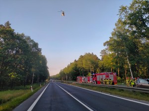 Zdjęcie przedstawia: Lotnicze Pogotowie Ratunkowe w powietrzu nad drogą. Na jezdni służby ratunkowe.