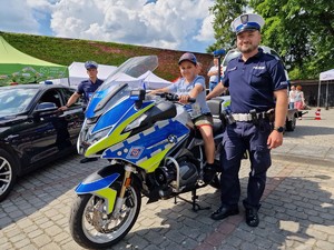 Zdjęcie przedstawia: umundurowanego policjanta z dzieckiem który siedzi na policyjnym motorze
