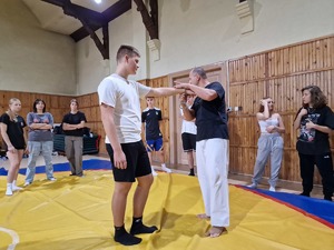 Zdjęcie przedstawia: instruktora i młodego chłopaka na macie podczas ćwiczeń kajdankowania.