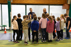 Zdjęcie przedstawia: policjantów i grupę dzieci na miasteczku ruchu drogowego, które mieści się na sali gimnastycznej.