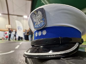 Zdjęcie przedstawia: policyjną czapkę ruchu drogowego, w tle miasteczko ruchu drogowego.